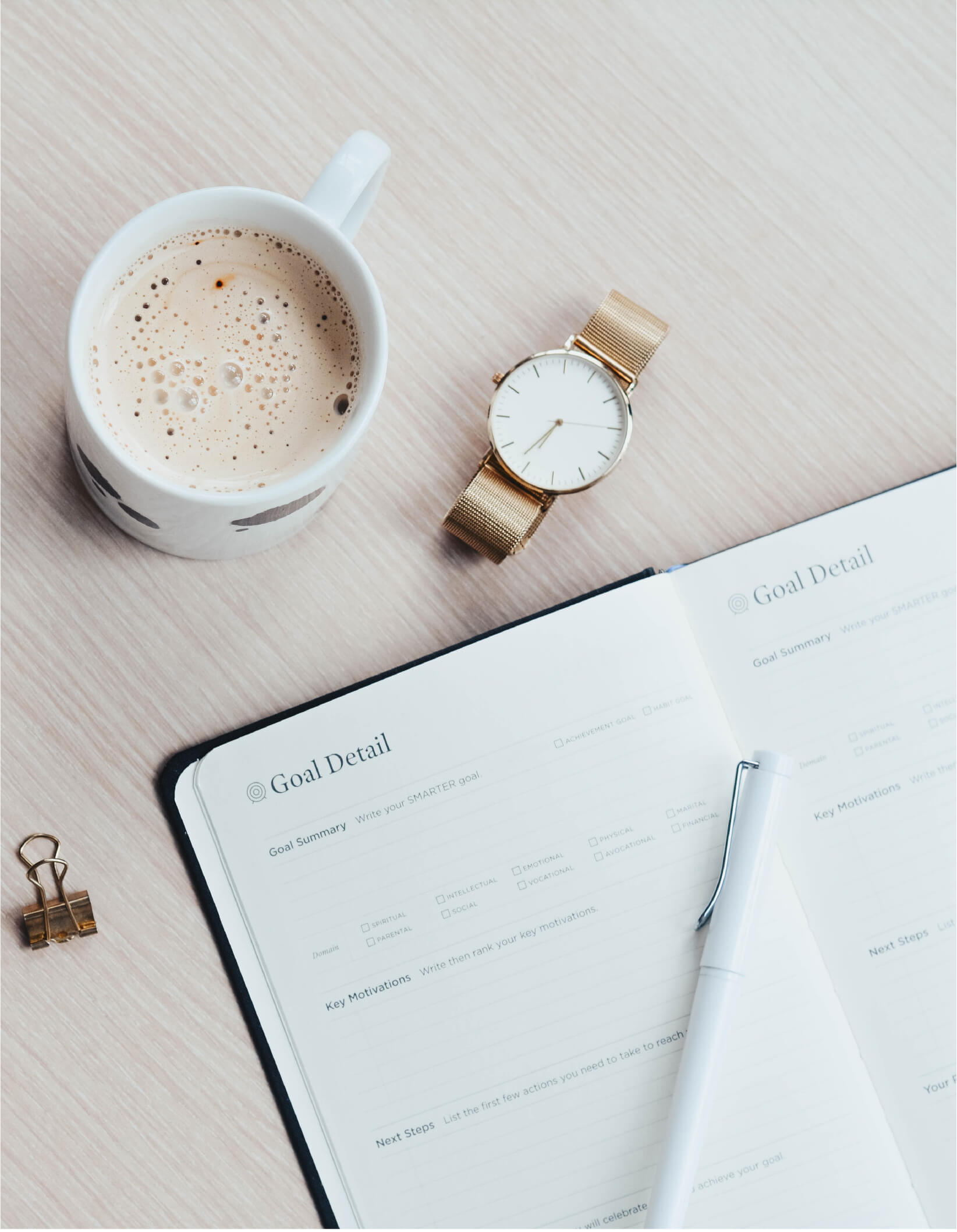 Photo of an open goal setting journal with a watch and a cup of coffee