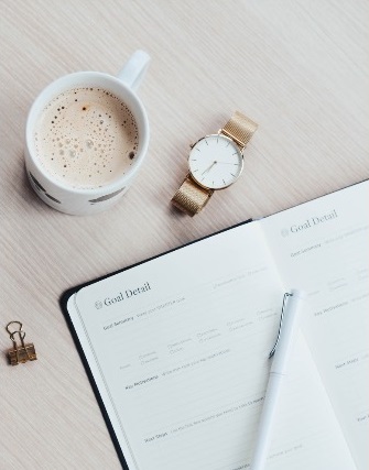 Photo of an open goal setting journal with a watch and a cup of coffee